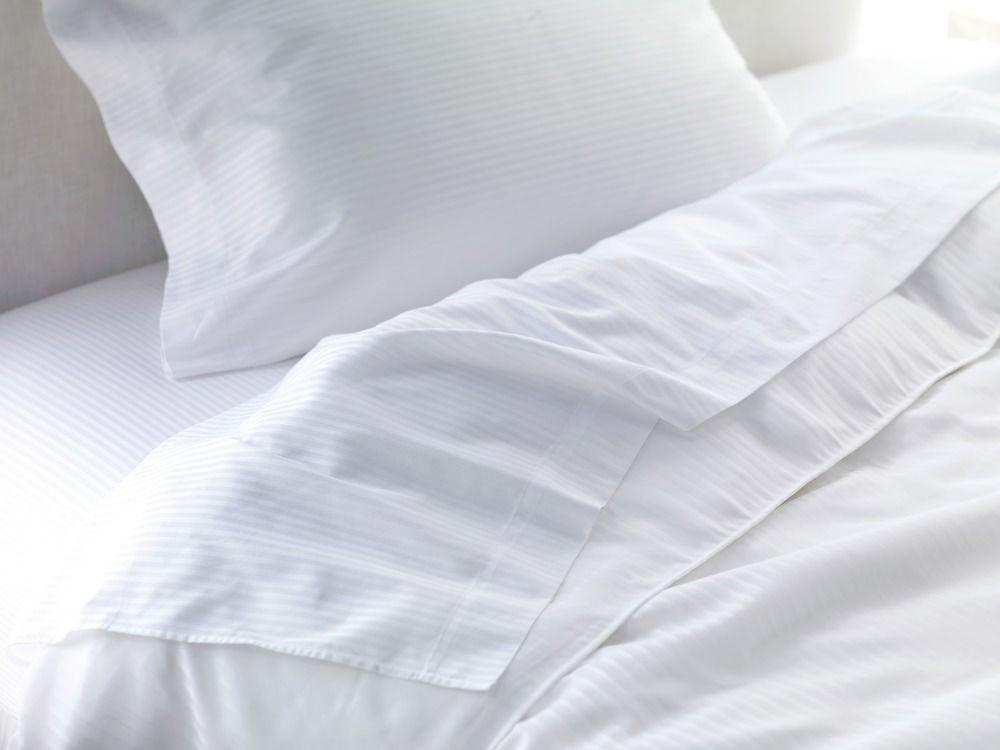 The Fullerton Hotel Sydney Eksteriør bilde The photo shows a neatly made bed with white bedding. There is a white pillow positioned at the top, and a light, textured blanket or duvet partially draped over the mattress, revealing a smooth white fitted sheet underneath. The overall aesthetic is