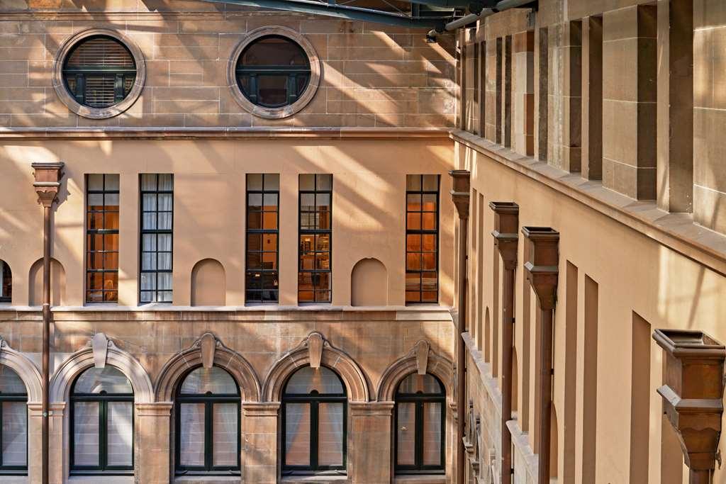 The Fullerton Hotel Sydney Interiør bilde The photo shows an architectural interior featuring a wall with large windows, showcasing a mix of rounded and rectangular shapes. The building materials appear to be a light-colored stone, and the play of light and shadow adds depth to the scene. Th