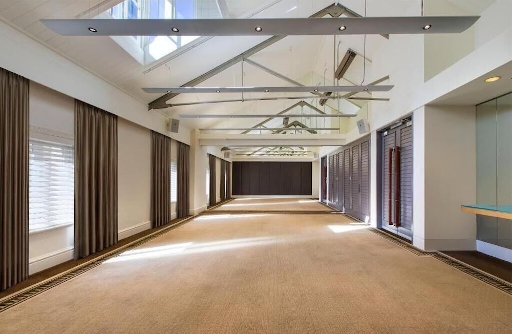 The Fullerton Hotel Sydney Eksteriør bilde The photo depicts a spacious interior room with a high ceiling featuring exposed beams. The flooring appears to be carpeted in a neutral color. Natural light floods the room through large windows and skylights, creating a bright atmosphere. On the si