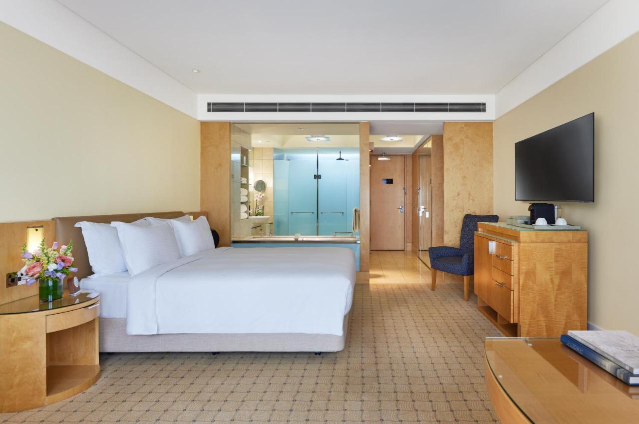 The Fullerton Hotel Sydney Eksteriør bilde The photo depicts a modern hotel room featuring two neatly made beds with white linens. The room has light-colored walls and a warm, inviting atmosphere. On one side, there is a wooden bedside table, and a bouquet of flowers adds a touch of color. A 