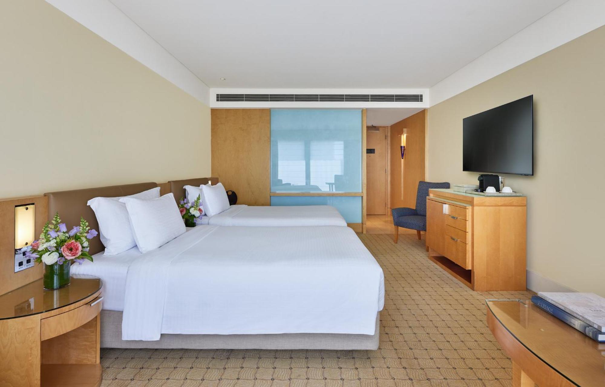 The Fullerton Hotel Sydney Eksteriør bilde The photo shows a hotel room with two beds, each made up with white linens and pillows. There are small flower arrangements on the side tables next to the beds. The room has a light color scheme with beige walls and wooden furniture. A blue glass par