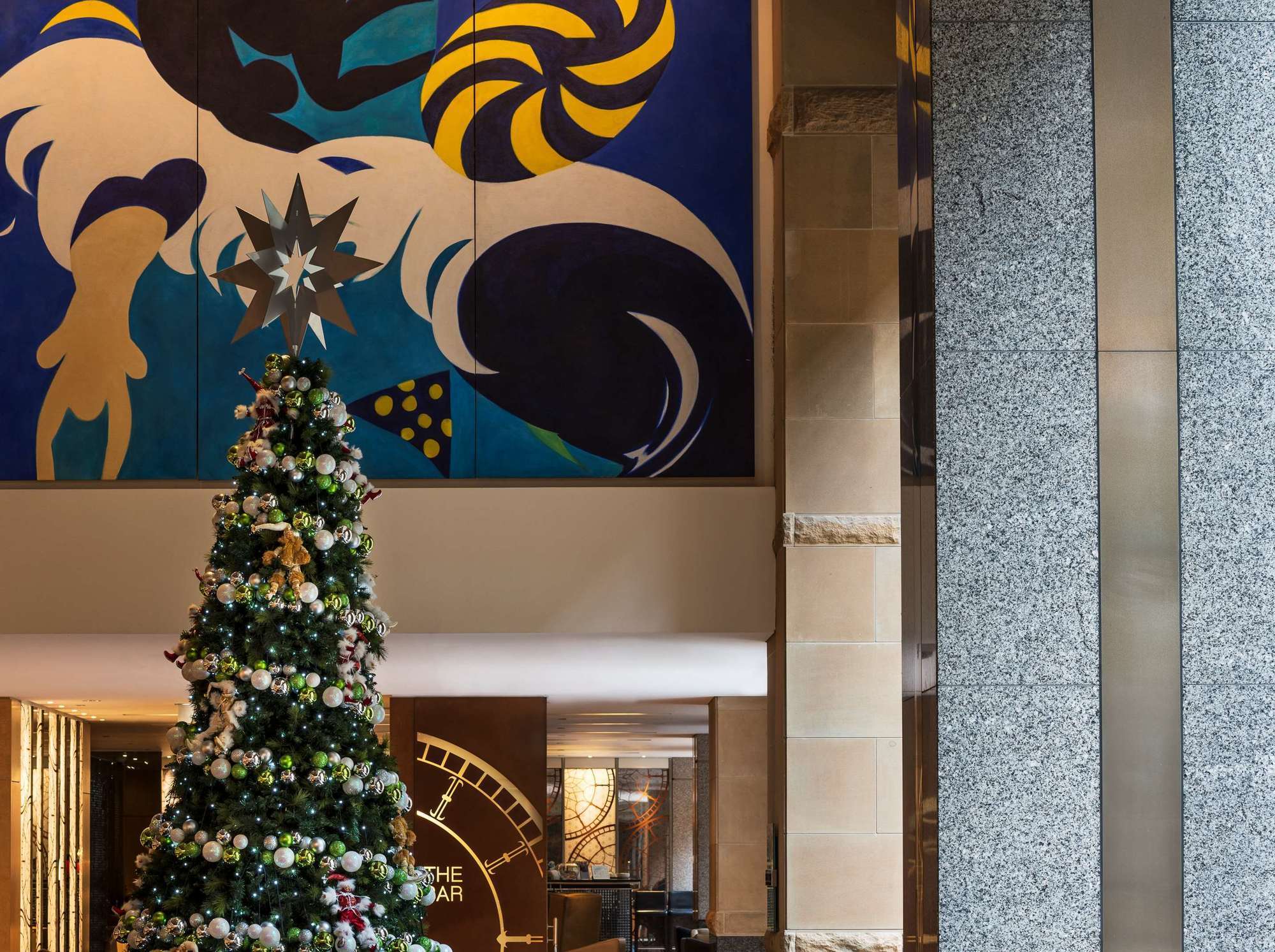 The Fullerton Hotel Sydney Eksteriør bilde The photo shows a bright and modern lobby area. In the foreground, there is a beautifully decorated Christmas tree, adorned with ornaments and lights. Behind the tree, there is a large and colorful mural featuring abstract shapes and vibrant colors. 