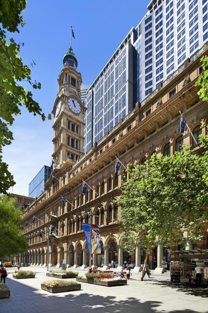 The Fullerton Hotel Sydney Eksteriør bilde The photo shows a historic building featuring a prominent clock tower. The architecture is characterized by ornate details and large windows. The structure has flags on display, and the foreground includes greenery, suggesting that it is set in an ur