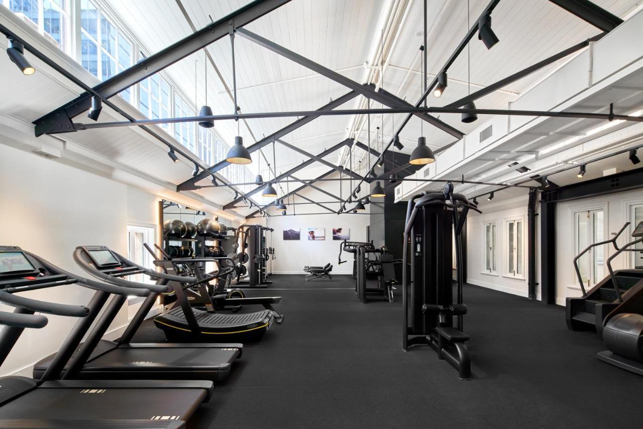 The Fullerton Hotel Sydney Eksteriør bilde The photo shows a modern gym interior with various exercise equipment. There are treadmills that line one side and strength training machines on the other. The gym features a high ceiling with exposed beams and large windows that bring in natural lig