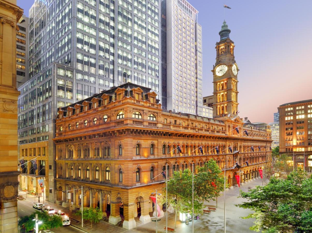 The Fullerton Hotel Sydney Eksteriør bilde The photo depicts a cityscape featuring a historical building with ornate architecture, prominently displaying a large clock tower. This structure is set against the backdrop of modern skyscrapers, highlighting a contrast between classic and contempo